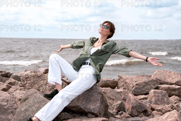 Portrait of a stylish woman sitting on stones in the bay. Windy weather. Happiness