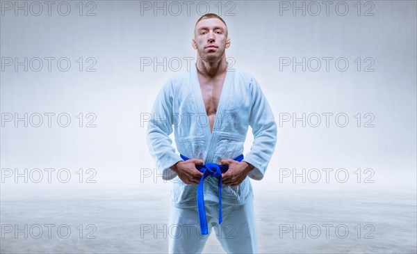 Athlete in a kimono with a blue belt stands on a light background. The concept of karate and judo.