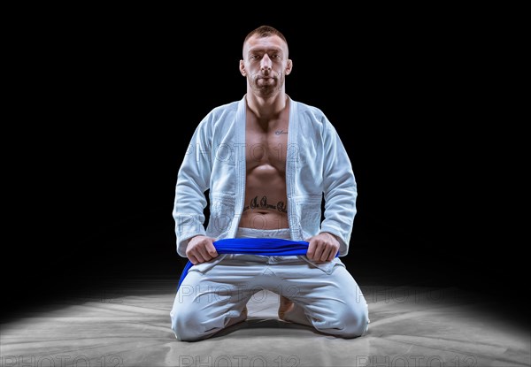 Professional athlete sits in the gym in a kimono with a blue belt. Concept of karate
