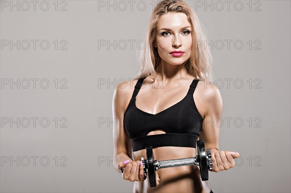 Charming athlete bends arm with dumbbell.