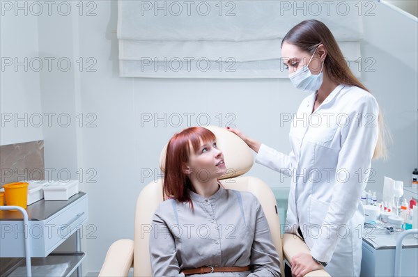 Beautician consults a woman in a beauty salon. The patient sits in a cosmetic chair and smiles at the specialist.