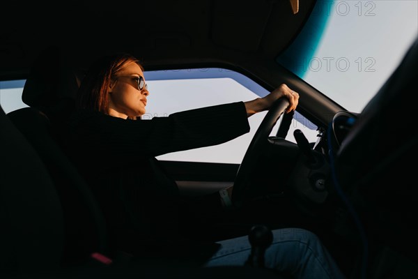 Young beautiful stylish girl driver in a jacket and sunglasses driving a car