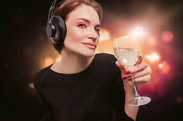 Image of a girl in a black dress with a glass of wine in her hand in a nightclub. Professional headphones. Party concept.