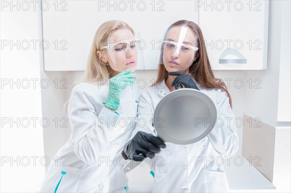 Two beauticians pose in a medical salon with a mirror in their hands. Rejuvenation concept.