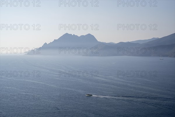 View of the misty Gulf of Porto with an excursion boat in the foreground and the Scandola nature reserve in the background