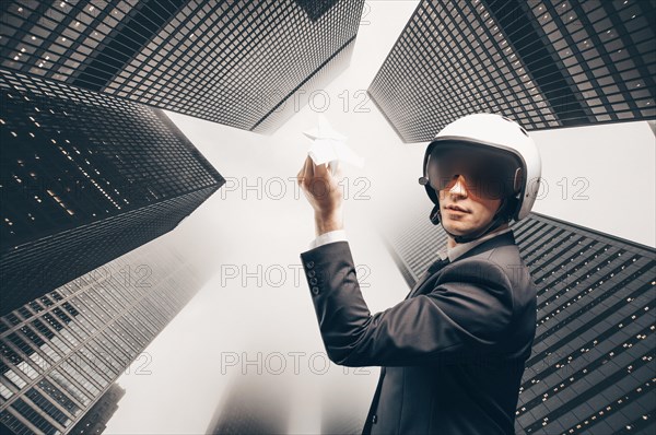 Portrait of a man in a suit and helmet. He launches a paper airplane up to the roofs of the skyscrapers of the financial district. Business concept.