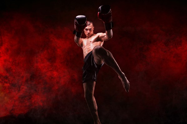 Professional kickboxer posing against a background of fire and smoke. Mixed martial arts. Sports concept