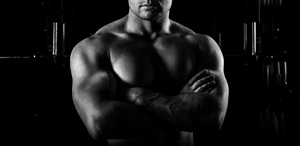 The weightlifter is posing in front of the camera with his arms crossed over his chest. Front view