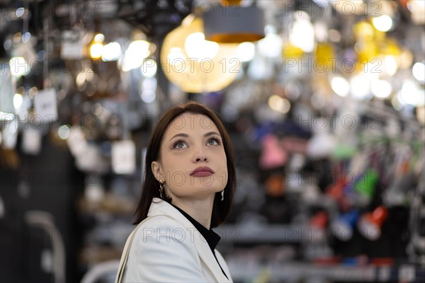 Beautiful young woman in a white jacket chooses a chandelier in a hardware store