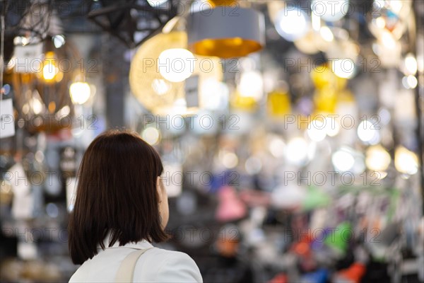 Beautiful young woman in a white jacket chooses a chandelier in a hardware store