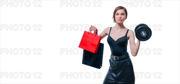 Beautiful slender woman posing in the studio with a dumbbell and gift bags. Gift concept. Gym membership