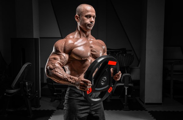 Muscular man posing in the gym with a barbell disc. Bodybuilding and powerlifting concept.