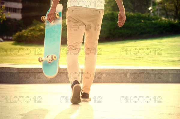 Guy with a skateboard strolls in a park under the scorching sunlight