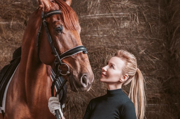 Stunning blonde posing with a thoroughbred horse. Ranch vacation concept.