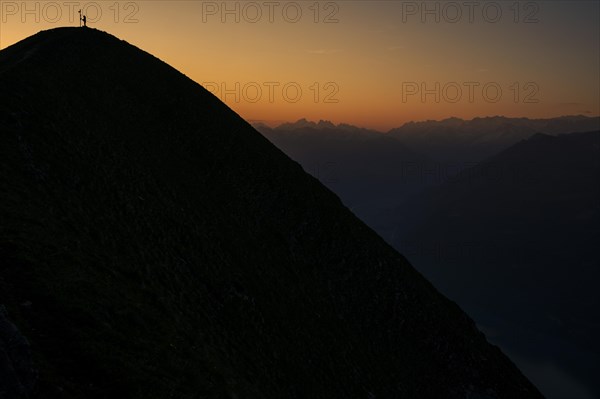 Mountaineer on ridge with Swiss mountains in the background at sunrise