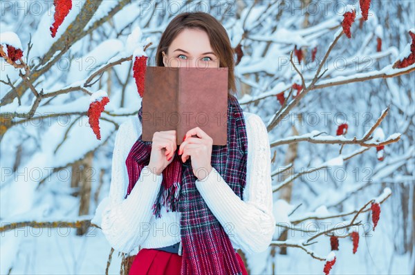 Portrait of a charming girl who reads a book in the winter forest. Concept of Christmas