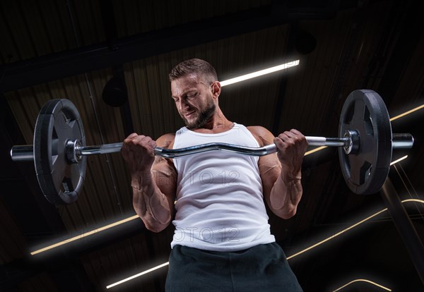 Image of a muscular guy in a white jersey with sports equipment. Gym. Fitness concept