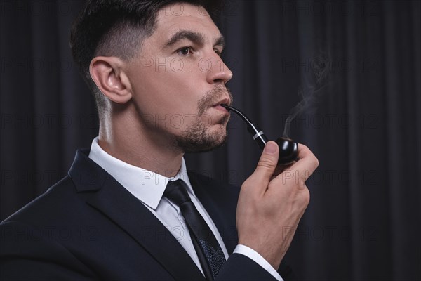 Image of an elegant man in a suit smoking a pipe. Business success concept.