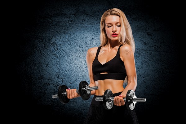 Sportive girl with an ideal figure posing in the studio with dumbbells in her hands.