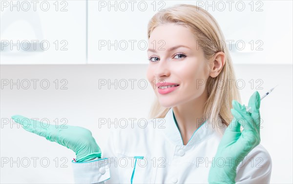 Portrait of a blonde girl in a medical gown with a syringe in her hands. Vaccination concept.