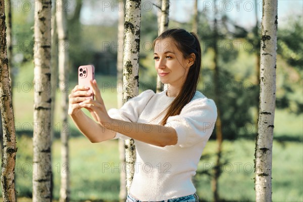 Influencer woman makes selfie on nature among birch trees