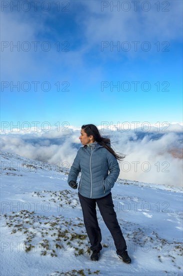 Middle-aged latina woman on a snow-capped mountain above the clouds