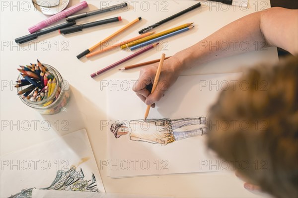 Top view of a fashion designer drawing a fashion sketch with colorful pencils