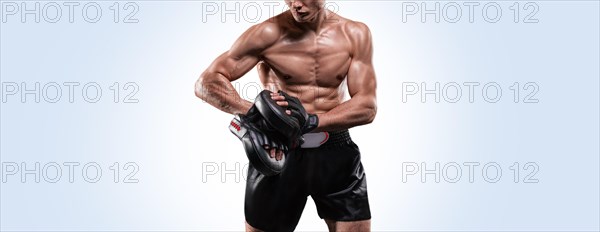 Muscular fighter posing with boxing paws in the studio on a light background. Mixed martial arts concept. High image quality