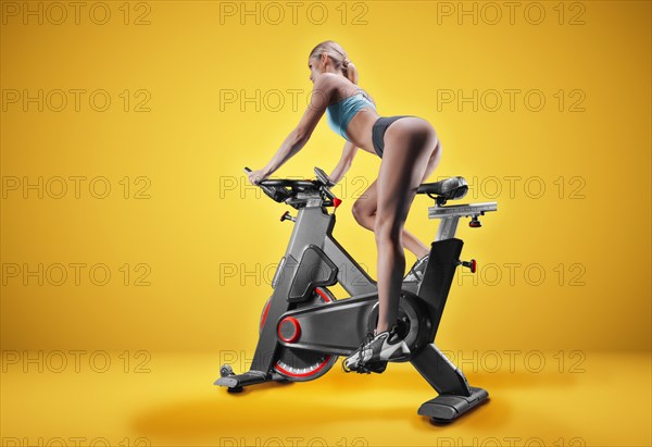 Long-legged girl posing in the studio on an exercise bike. Orange background. The concept of sports