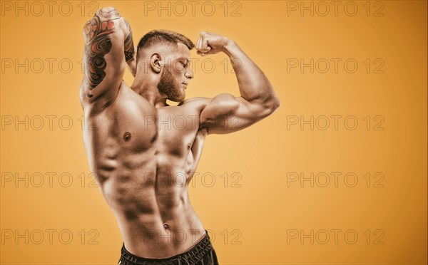 Young muscular guy with nice abs posing on an orange background. Fitness and nutrition concept.