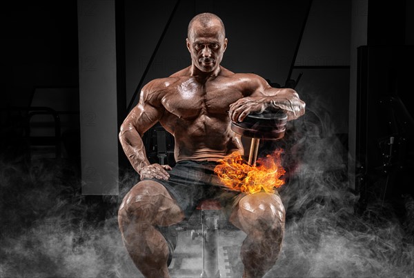 Muscular man sits on a bench with dumbbells burning. Bodybuilding and powerlifting concept.