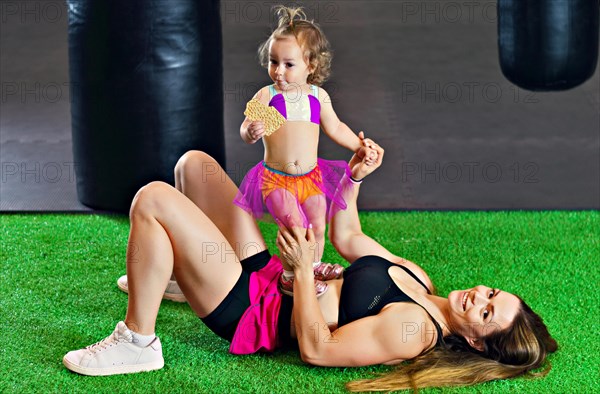 Charming sports mom plays in the gym with her little daughter.