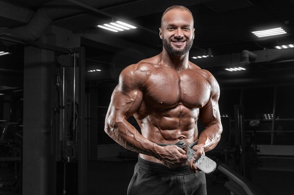 The athlete poses in the gym with an athletic belt. Fitness