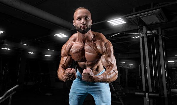 Muscular man in jeans poses in the gym. Sports