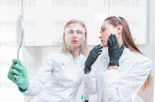 Two beauticians pose in a medical salon with a mirror in their hands. Rejuvenation concept.