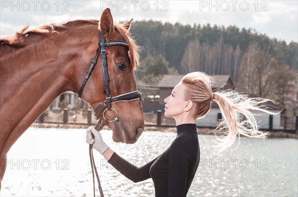 Beautiful stylish woman walking with a horse in a country club. Equestrian sport