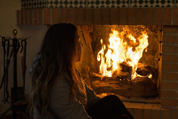 Latin woman sitting in front of the fireplace in the cold winters