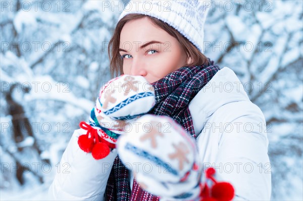 Portrait of a beautiful woman against the background of a winter forest in New Year's mittens. Concept of Christmas