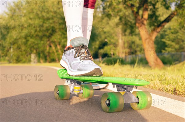 Images of a leg standing on a skateboard. Sunny evening in the park. Skateboarding concept.