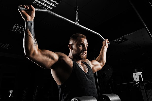 Professional athlete performs an exercise in the gym. Pulls the bar to the back of the head. Exercise for development of back muscles