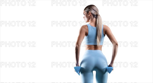 Slender athletic girl in a blue tights posing with dumbbells. Back view.