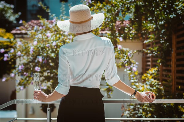 Elegant girl in a wide-brimmed hat has entered the terrace of a country house and looks at the garden. The concept of rest