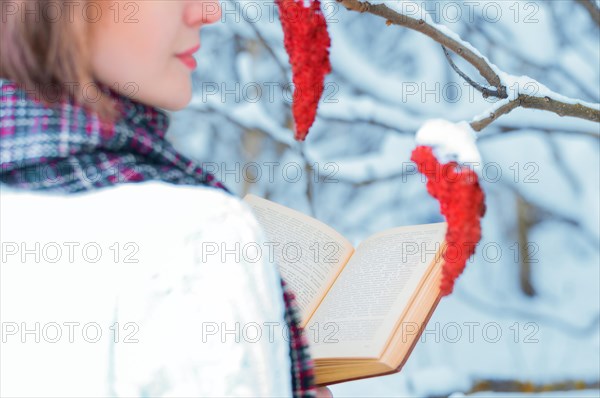 Portrait of a charming girl who reads a book in the winter forest. Concept of Christmas