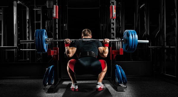 Professional athlete sits with a barbell on his shoulders and prepares to stand with her. View from the back