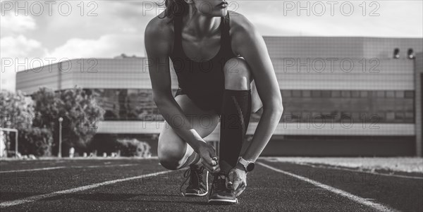 Image of a young female runner laces her shoes on a stadium track. Sports concept.