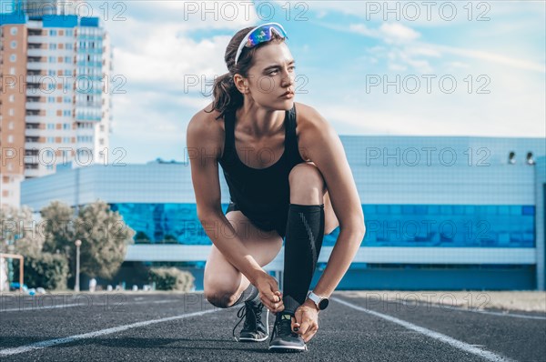 Image of a young female runner laces her shoes on a stadium track. Sports concept.