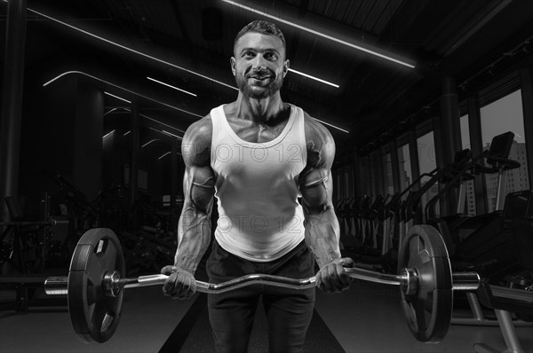 Handsome young man working out with a barbell in the gym. Biceps pumping. Fitness and bodybuilding concept.