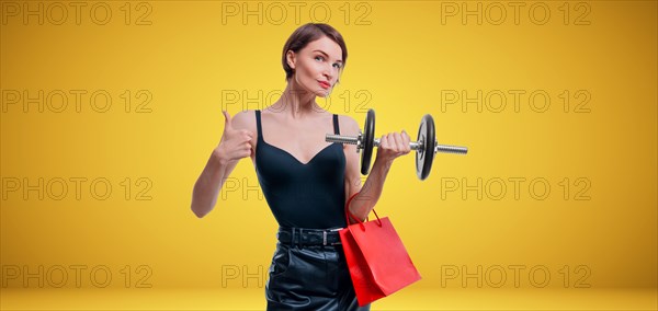 Beautiful slender woman posing in the studio with a dumbbell and gift bags. Gift concept. Gym membership. Ok sign.