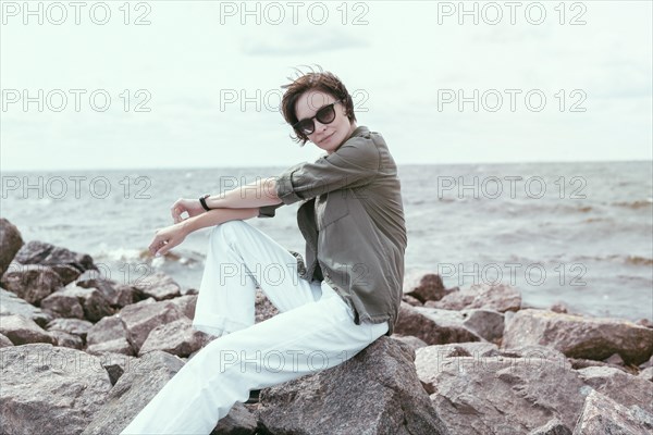 Portrait of a stylish woman sitting on stones in the bay. Windy weather. Happiness