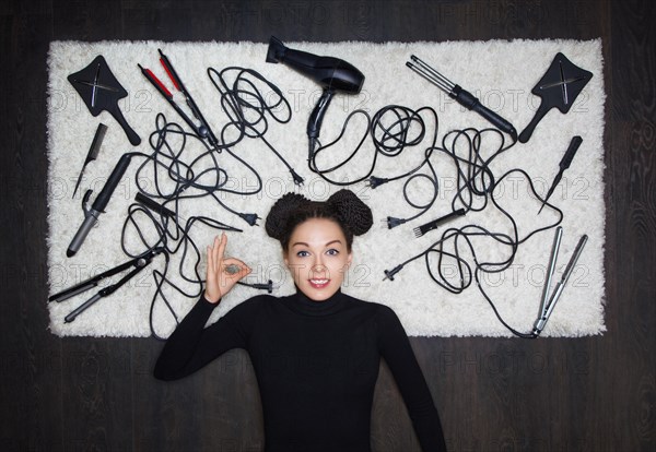 Young and charming girl with dreadlocks on her head shows an OK sign. The girl is lying on a white carpet. Around the tools for creating a